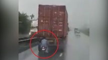 Nam thanh niên đi xe máy núp sau container để tránh mưa