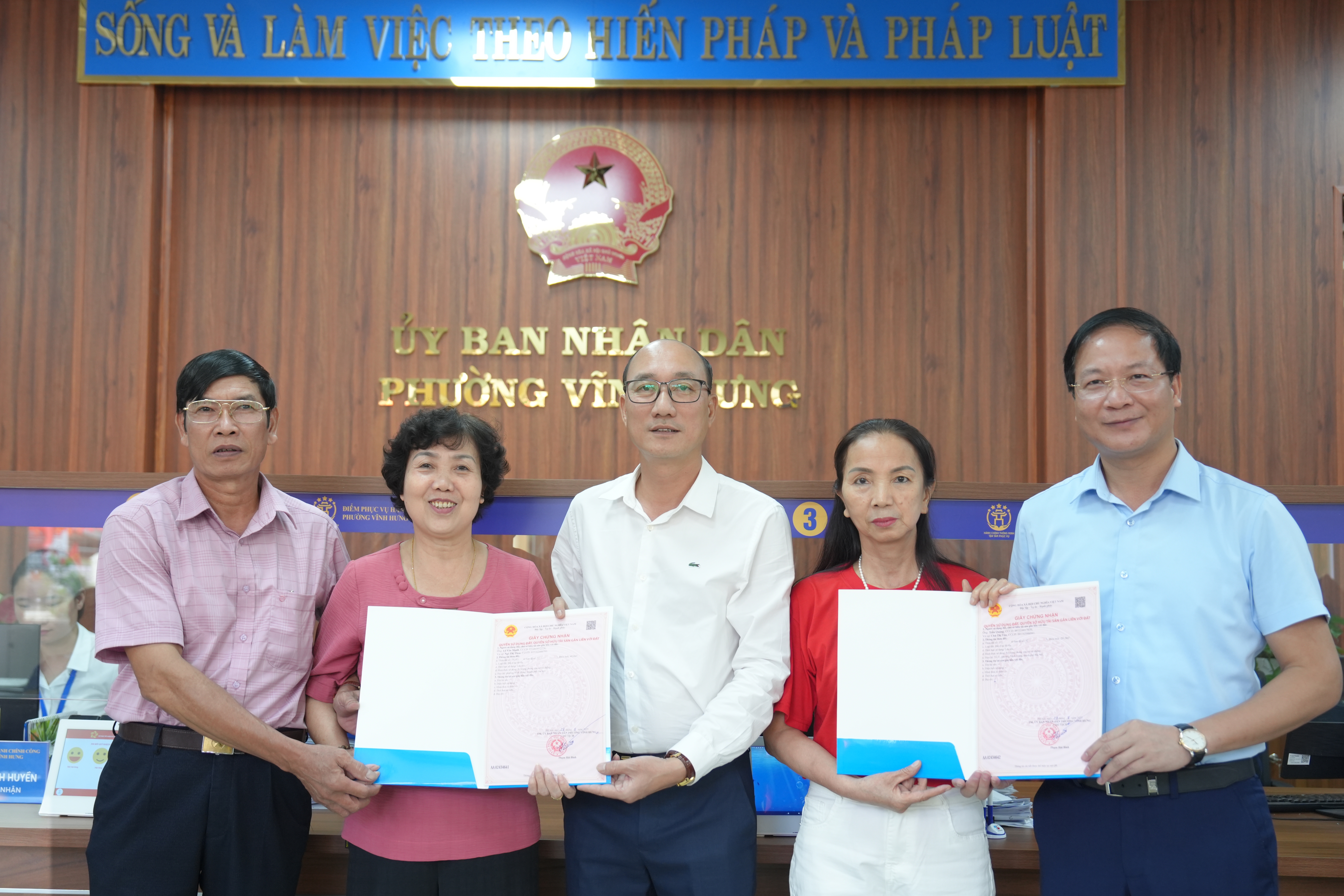 Bí thư Đảng ủy, Chủ tịch HĐND phường Vĩnh Hưng Nguyễn Đức Dũng và Chủ tịch UBND phường Vĩnh Hưng Phạm Hải Bình trao sổ đỏ cho gia đình bà Chử Thị Tân (bên phải) và ông Lê Văn Mạnh - bà Ngô Thị Thoa (bên trái)