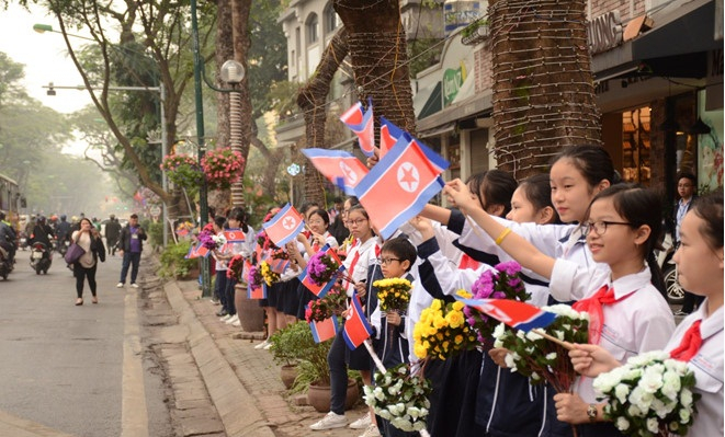 các em học sinh cầm cờ Triều Tiên đứng bên đường chào đón lãnh đạo Kim Jong-un.